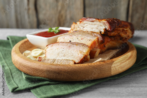 Pieces of baked pork belly served with sauce on grey wooden table, closeup