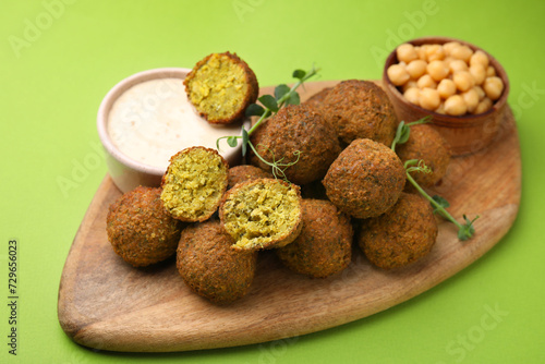 Delicious falafel balls, chickpeas and sauce on green background