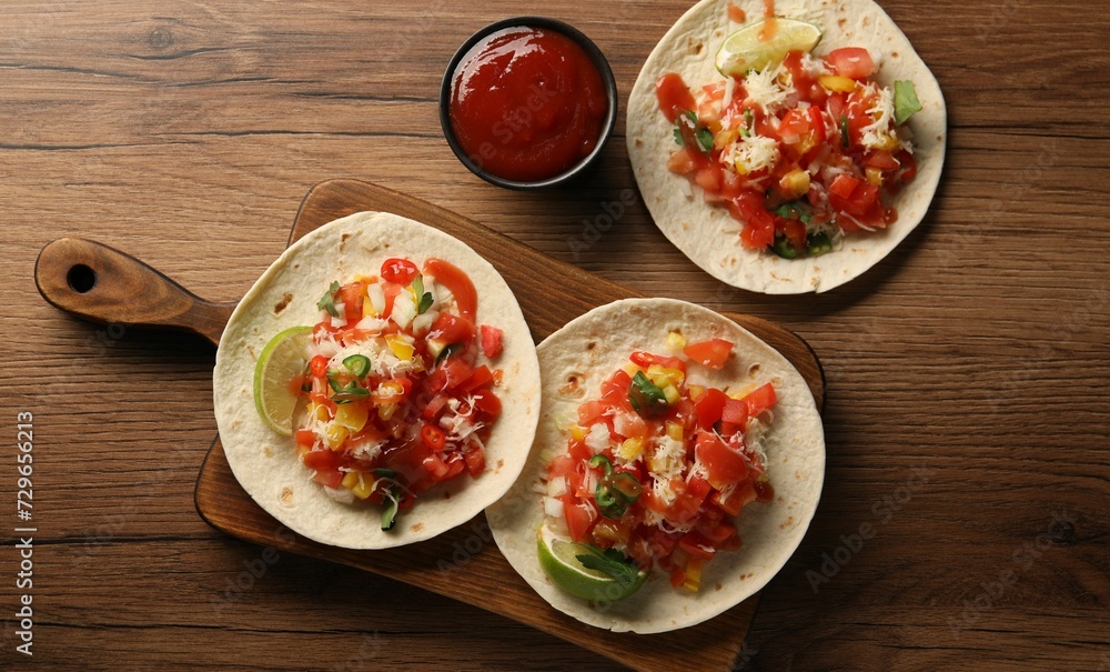 Delicious tacos with vegetables, lime and ketchup on wooden table, flat lay