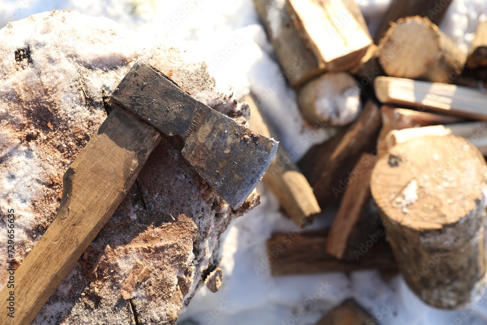 Metal axe on wooden log and pile of wood outdoors on sunny winter day, top view. Space for text Metal axe on wooden log and pile of wood outdoors on sunny winter day, top view. Space for text
