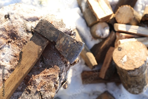 Metal axe on wooden log and pile of wood outdoors on sunny winter day, top view. Space for text