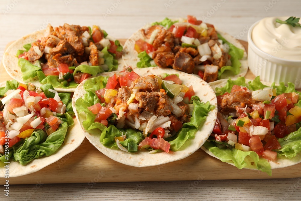 Delicious tacos with vegetables, meat and sauce on white wooden table