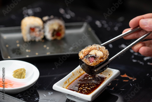 Close up of hands with chopsticks eating japanese food. Traditional asian rolls. Maki sushi with vegetables and tuna