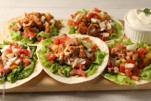 Delicious tacos with vegetables, meat and sauce on white wooden table