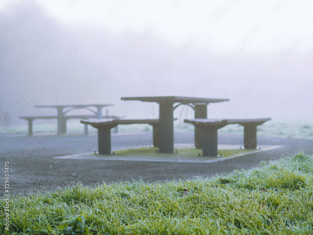 Modern metal bench and table with plastic elements in a park, fog in the background over green field. Surreal mood. Calm nature scene with mist Modern metal bench and table with plastic elements in a park, fog in the background over green field. Surreal mood. Calm nature scene with mist