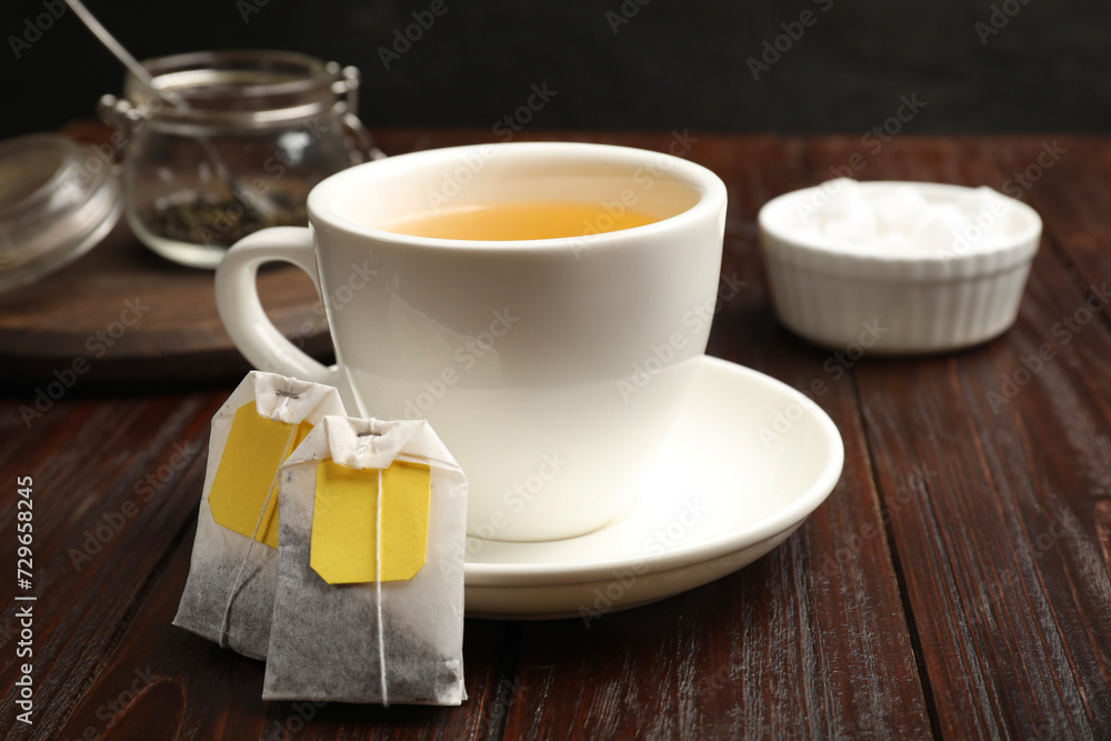 Tea bags and cup of hot beverage on wooden table, closeup Tea bags and cup of hot beverage on wooden table, closeup