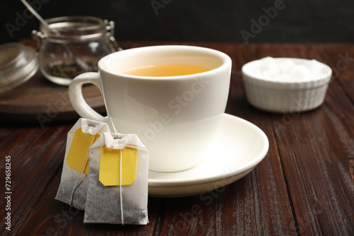 Tea bags and cup of hot beverage on wooden table, closeup