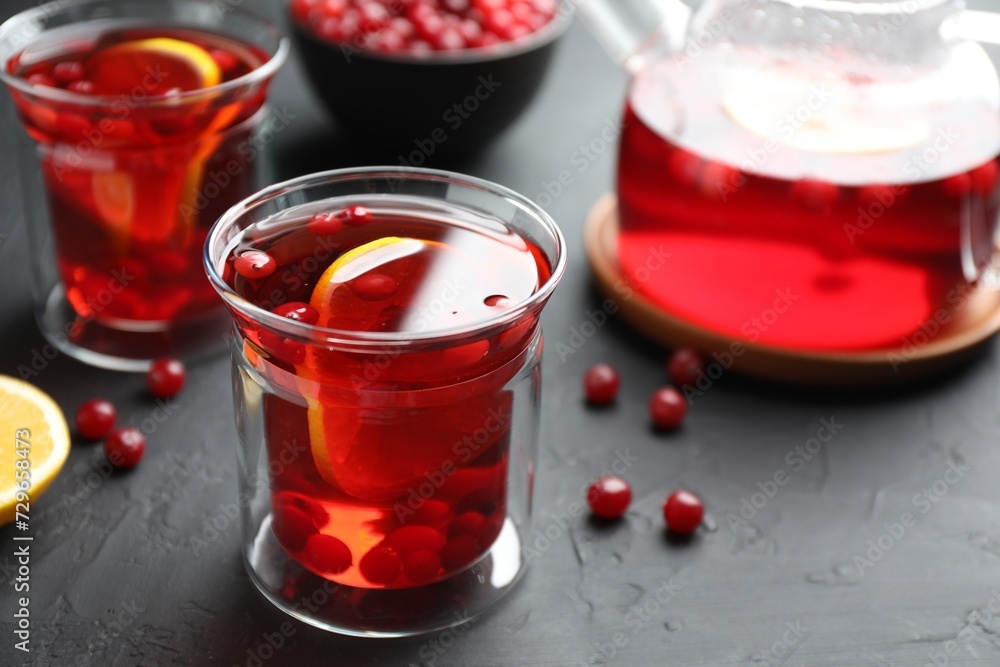 Tasty hot cranberry tea with lemon and fresh berries in glass on black textured table Tasty hot cranberry tea with lemon and fresh berries in glass on black textured table