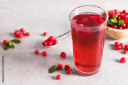 Tasty cranberry juice in glass and fresh berries on light grey table