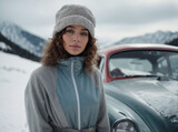 A beautiful woman in vintage style stands near a car against a background of snowy mountains.