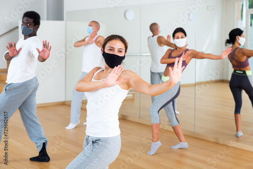 Dance class for adults during coronavirus outbreak, positive young adult men and women in face masks training in dance studio