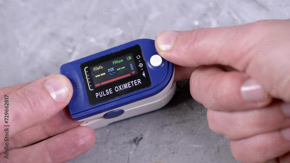 Woman Measures Pulse and Oxygen Saturation Using a Pulse Oximeter at Home. Close-up. Grey background. A dial with sensors and indicators on the device. Measurement of heart rate, pulse, heartbeat. Woman Measures Pulse and Oxygen Saturation Using a Pulse Oximeter at Home. Close-up. Grey background. A dial with sensors and indicators on the device. Measurement of heart rate, pulse, heartbeat.