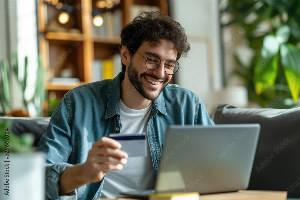Smiling man with glasses making an online payment on a laptop with a credit card Smiling man with glasses making an online payment on a laptop with a credit card