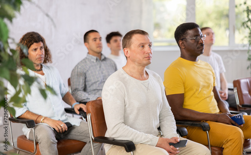Small group of mature guys attending the lecture with concern sitting on chairs in light room