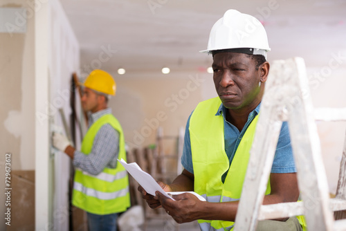 African-american foreman with documents, analyzing plan of renovation works in apartment. photo