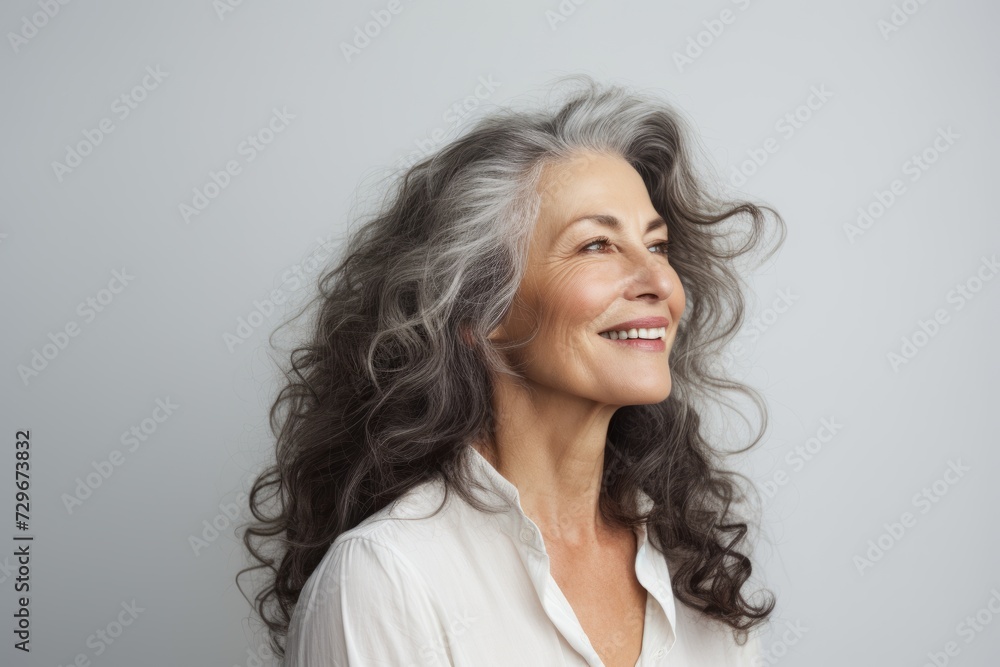 Portrait of a smiling senior woman with long gray hair on grey background
