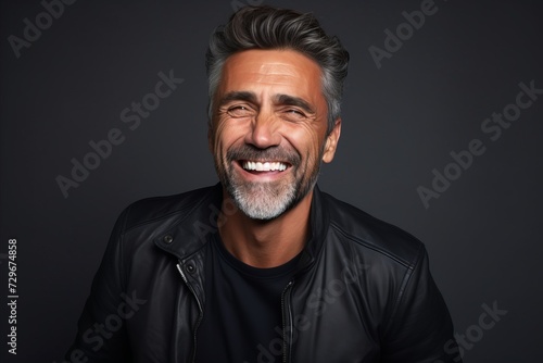 Portrait of a handsome middle-aged man laughing and looking at the camera while standing against grey background
