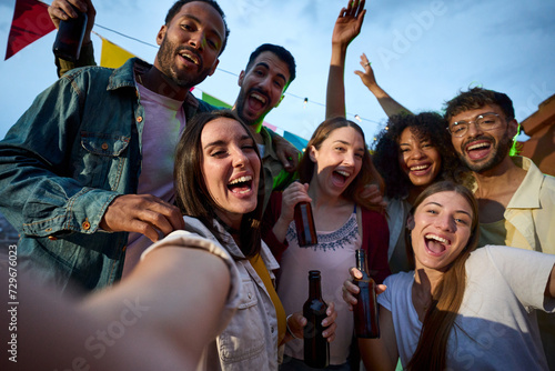 Cheerful attractive young woman taking selfie at millennial alcohol party surrounded by group happy multiracial friends posing outdoor looking excited at camera . Joyful people at night celebration
