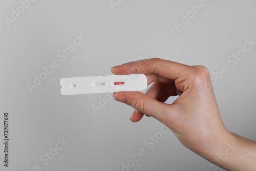 Woman holding disposable Covid-19 express test on light grey background, closeup