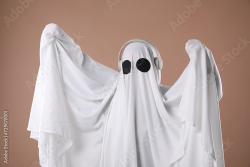 Person in ghost costume wearing headphones on dark beige background