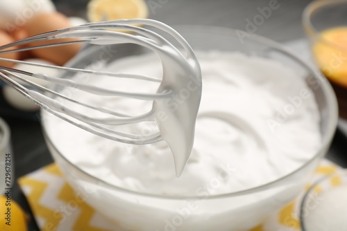 Whisk with whipped cream over bowl, closeup