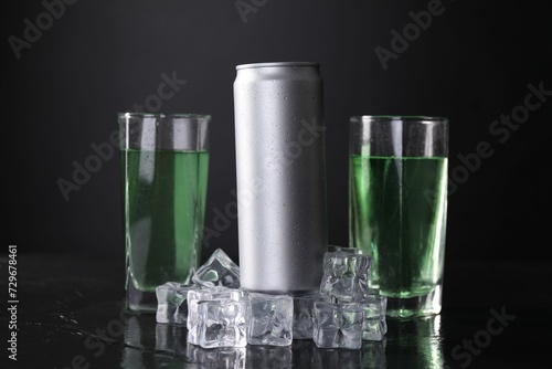Energy drink in glasses, aluminium can and ice cubes on black table