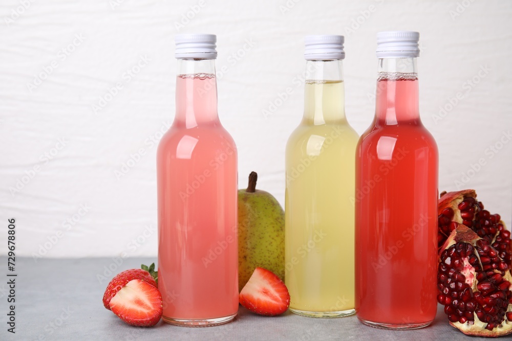 Delicious kombucha in glass bottles and fresh fruits on grey table against white background Delicious kombucha in glass bottles and fresh fruits on grey table against white background