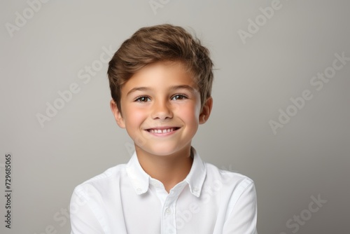 Portrait of a smiling little boy in a white shirt on a gray background