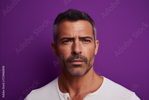 Portrait of serious mature man looking at camera and standing against purple background © Igor