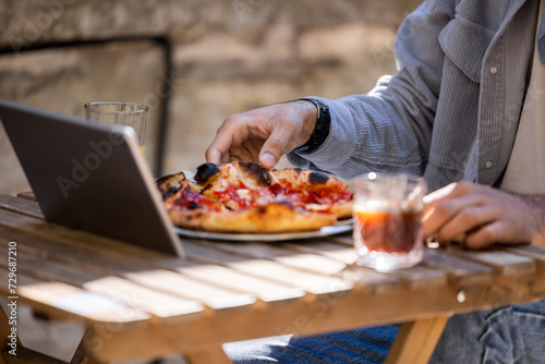 Man sitting at the table, eating pizza and working on laptop
