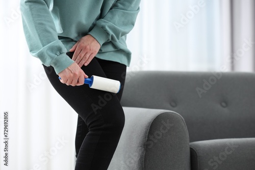 Woman with lint roller removing pet hair from black trousers indoors, closeup. Space for text