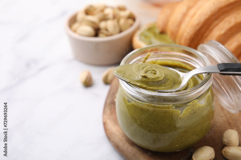 Tasty pistachio cream in jar, nuts and spoon on white marble table, closeup. Space for text Tasty pistachio cream in jar, nuts and spoon on white marble table, closeup. Space for text
