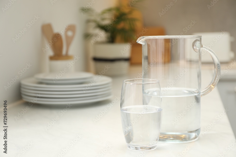 Jug and glass with clear water on white table in kitchen, space for text Jug and glass with clear water on white table in kitchen, space for text
