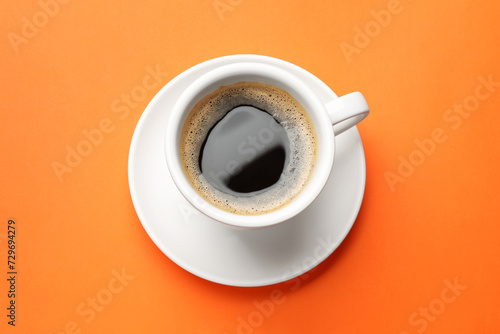 Fresh coffee in cup on orange background, top view