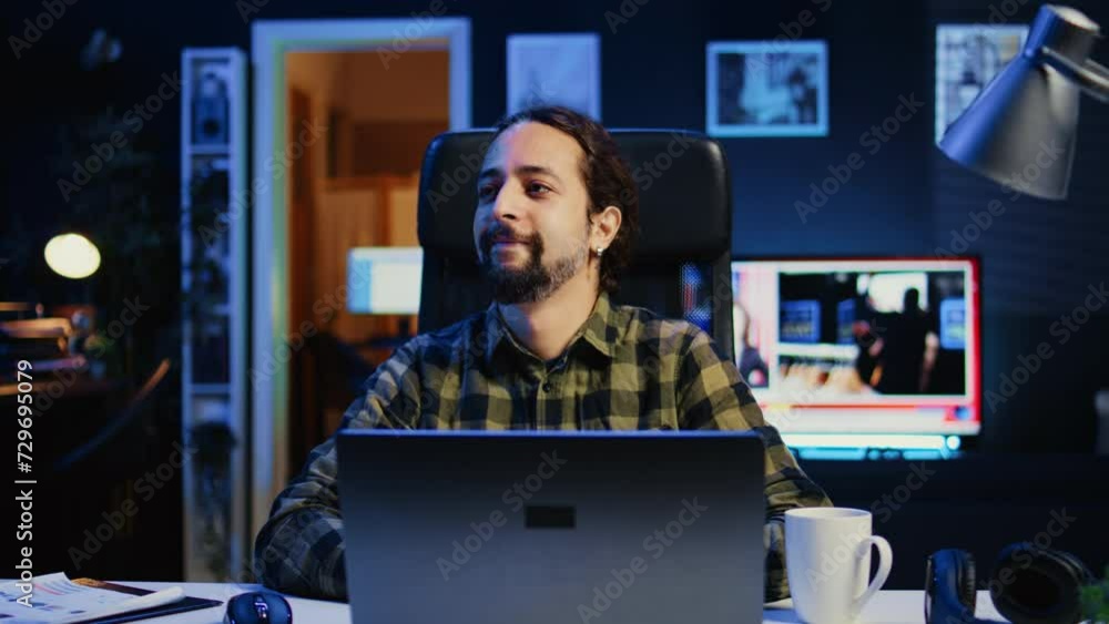 Portrait of happy man sitting at home office desk, preparing to solve tasks on laptop. Cheerful freelancer in front of digital device, doing email communication in living room, camera B Portrait of happy man sitting at home office desk, preparing to solve tasks on laptop. Cheerful freelancer in front of digital device, doing email communication in living room, camera B
