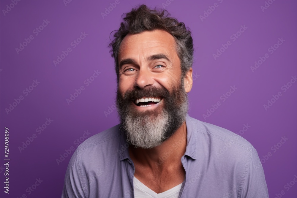 Portrait of happy mature man with beard and mustache looking at camera and laughing while standing against purple background Portrait of happy mature man with beard and mustache looking at camera and laughing while standing against purple background