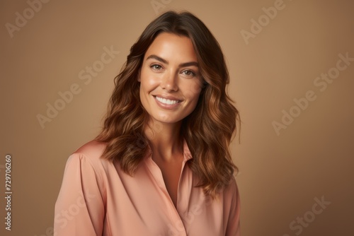 Portrait of a beautiful young woman smiling at camera while standing against brown background