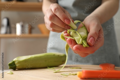 Woman with peels of fresh zucchini at table in kitchen, closeup. Space for text