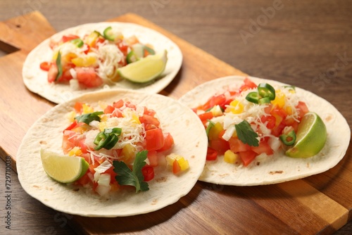 Delicious tacos with vegetables and lime on wooden table, closeup