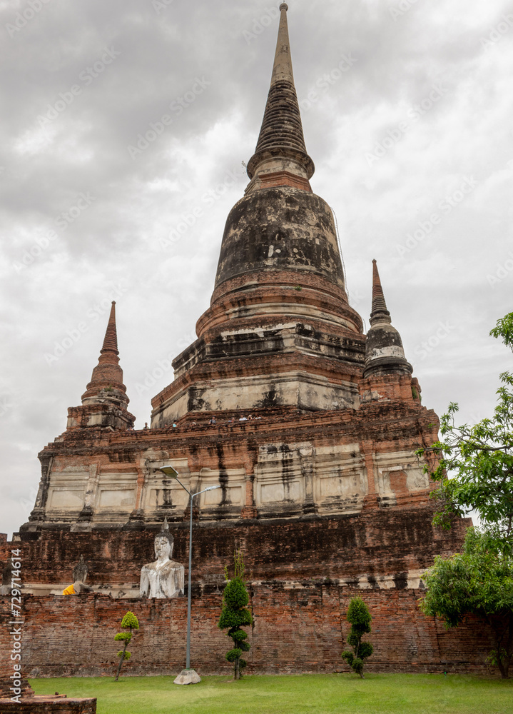 Fototapeta premium Stone Buddha statue and Thai buddhist red brick temple Pagoda at the Wat Wat Yai Chai Mongkhon historical site in Ayutthaya Thailand on a cloudy day