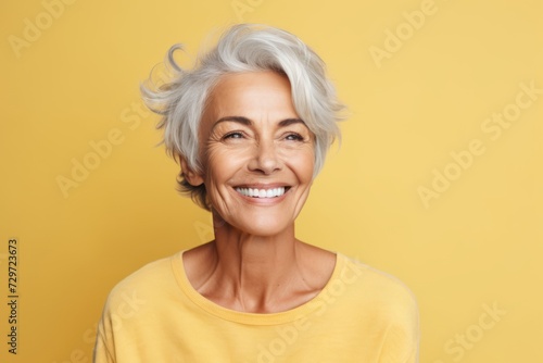 Close up portrait of a happy senior woman looking at camera over yellow background