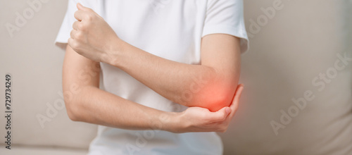 Photography Woman having elbow ache during sitting on couch at home, muscle pain due to lateral epicondylitis or tennis elbow