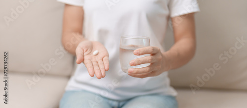 woman hand holding medicine painkiller pill and water glass on the sofa at home, taking for headaches,  stomach ache, Diarrhea Pain from food poisoning, Endometriosis, Hysterectomy and Menstrual