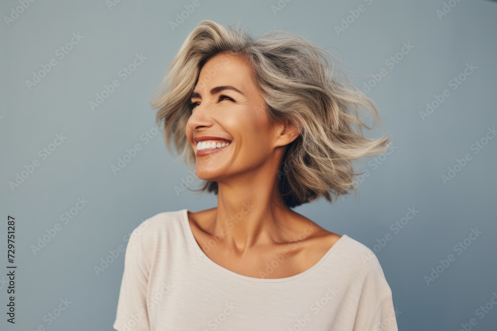smiling middle aged woman with grey hair looking up over grey background smiling middle aged woman with grey hair looking up over grey background