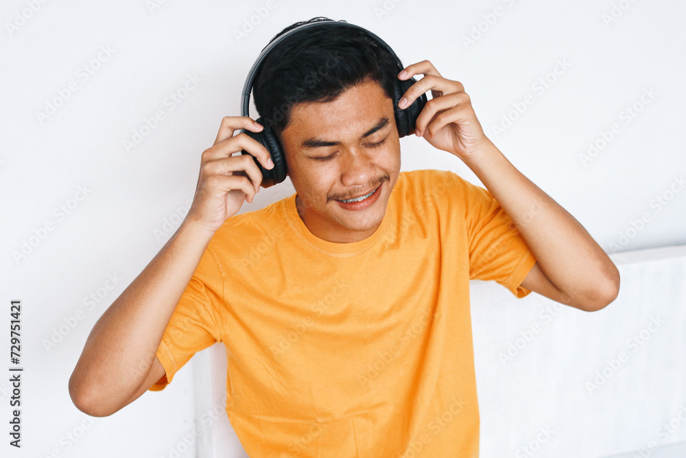 Happy young Asian teenage boy with braces wearing headphones and enjoying listening music Happy young Asian teenage boy with braces wearing headphones and enjoying listening music