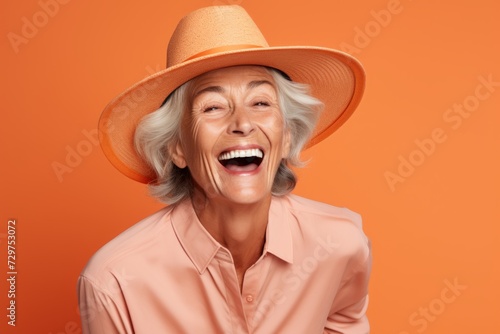 Portrait of happy senior woman in hat and shirt on orange background