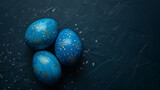 Three hand-painted blue Easter eggs with gold accents on a dark textured background, symbolizing the Easter holiday, background with a place for text