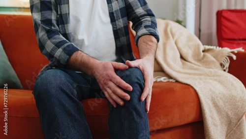 Unrecognizable middle-aged man suffer from painful discomfort severe knee joint ache leg muscles could not walk. Sick guy massaging knees illness cramps rheumatism at home on sofa. Health care problem photo