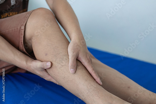 Close-up of an elderly man holding his leg in discomfort. Suffering from pain while sitting in bed  elderly and health concept  arthritis  pain  touch leg and feel pain in leg.