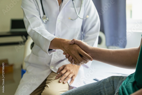 Doctor and patient shaking hands in the office, they are sitting at desk, hands close up A close - up handshake between a doctor and a patient in a medical office with clean